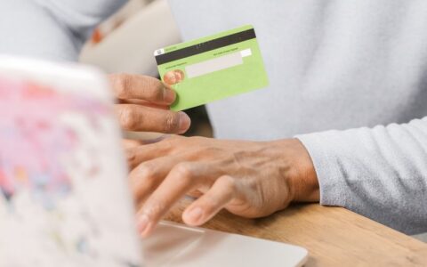 Close-up of hands holding a green credit card for an online purchase using a laptop, depicting secure transactions.